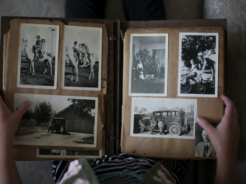 Hands opening an old family photo album filled with black and white photographs