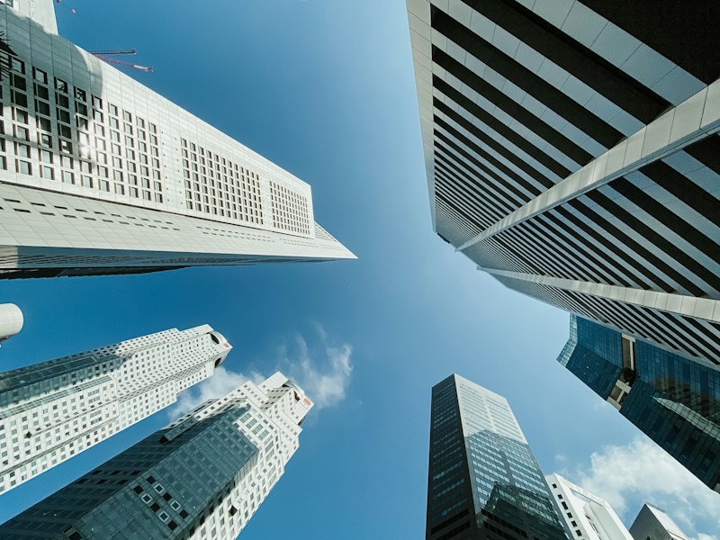 Looking up at glass and concrete office towers in Singapore's central business district against a blue sky