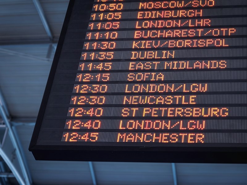 Low-angle view of an airport departure board listing flight times and destinations including Edinburgh, London, Dublin and Manchester