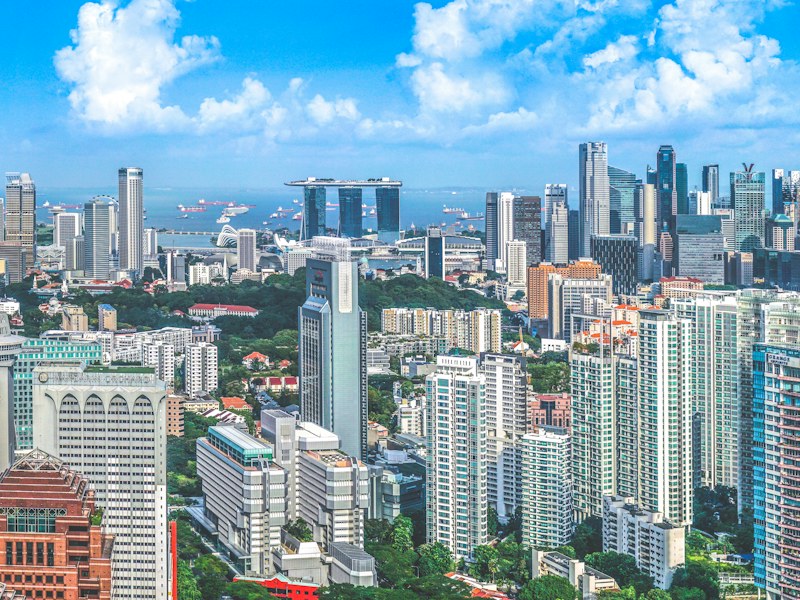 Singapore skyline on a clear day, with residential and office towers in the foreground and Marina Bay Sands and ships in the Singapore Strait in the distance
