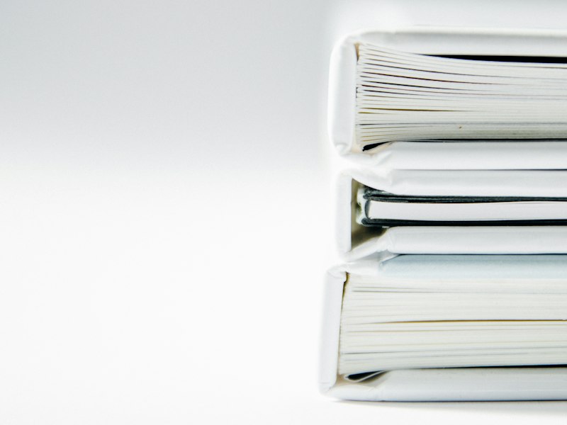 Stack of three thick white ring-binder folders full of paper against a plain white background