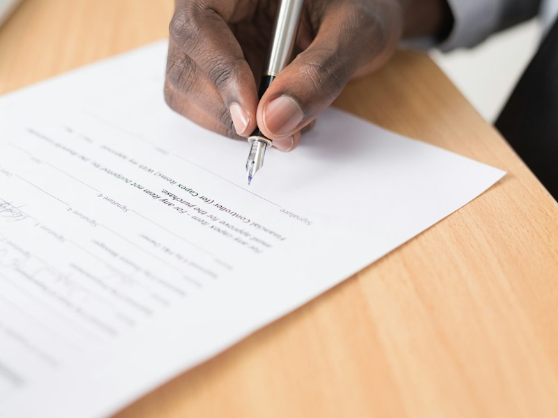 Close-up of a hand signing a printed document with a silver fountain pen on a wooden desk