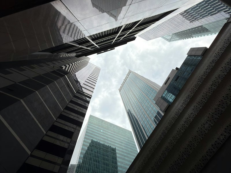 Looking up between glass and steel office towers at Raffles Place, Singapore, against an overcast sky