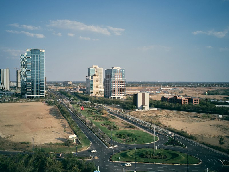 Aerial view of GIFT City, Gandhinagar, with glass office towers, a roundabout and open land under a blue sky