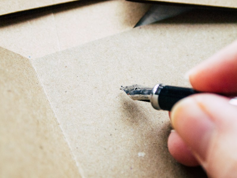 Hand holding a fountain pen poised to write on brown paper