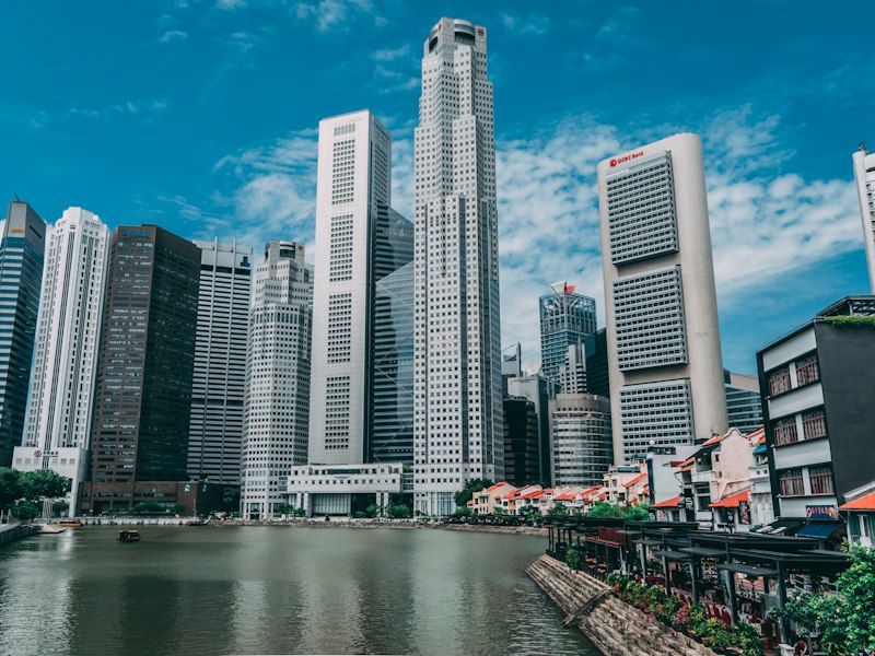 Office towers of Singapore's Raffles Place financial district rising behind the shophouses of Boat Quay on the Singapore River under a blue sky