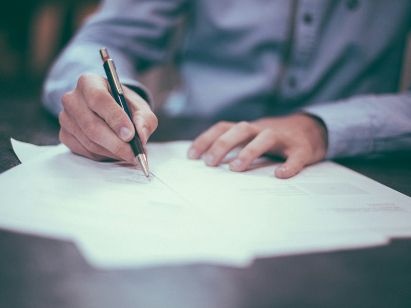 Close-up of a hand signing a printed document with a pen at a desk