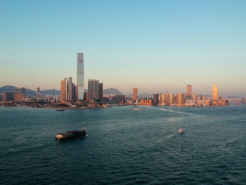 Kowloon skyline across Victoria Harbour in Hong Kong at sunset, with a barge and small boats on the water