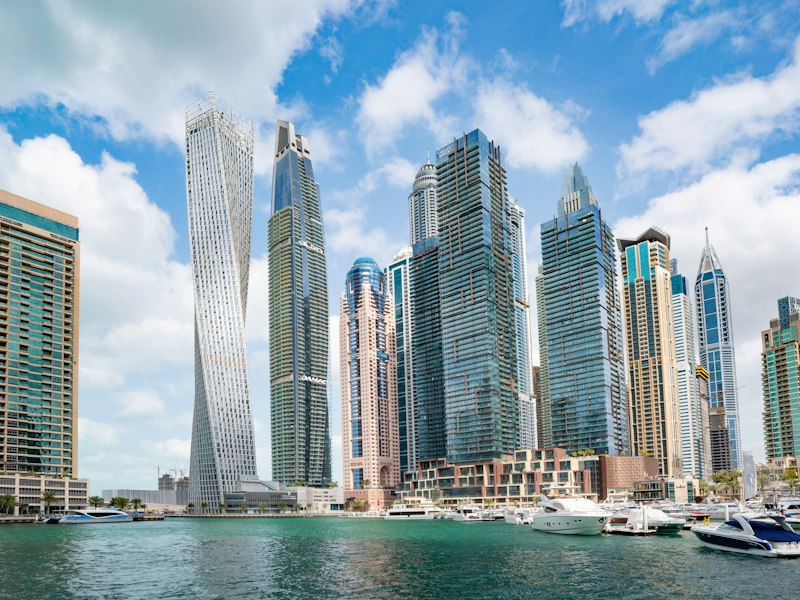 Dubai Marina skyline with a twisting skyscraper and other high-rise towers behind moored yachts on a sunny day