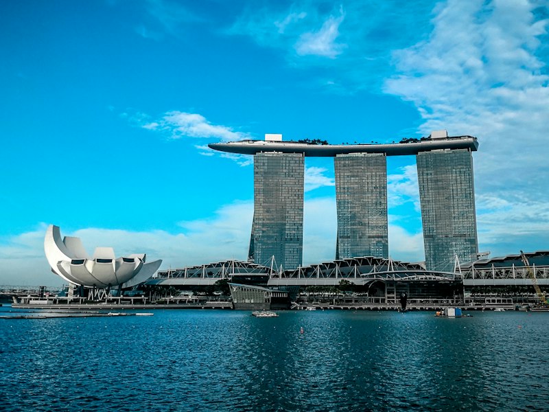 Marina Bay Sands towers and the lotus-shaped ArtScience Museum seen across the water of Marina Bay, Singapore, under a blue sky