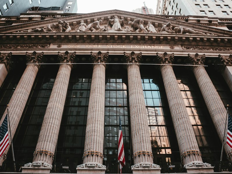 Facade of the New York Stock Exchange building on Wall Street with fluted columns, a carved pediment and US flags