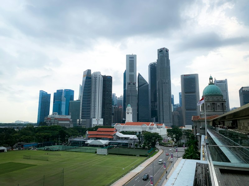 Raffles Place skyscrapers under a cloudy sky beyond the Padang playing field, with the green dome of the former Supreme Court building on the right